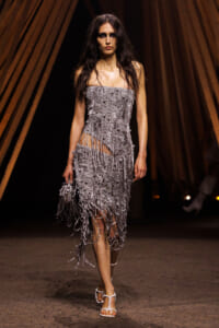 Model walking runway in a silver, bead- and fringe-covered strapless dress with a high-low fringe hem.