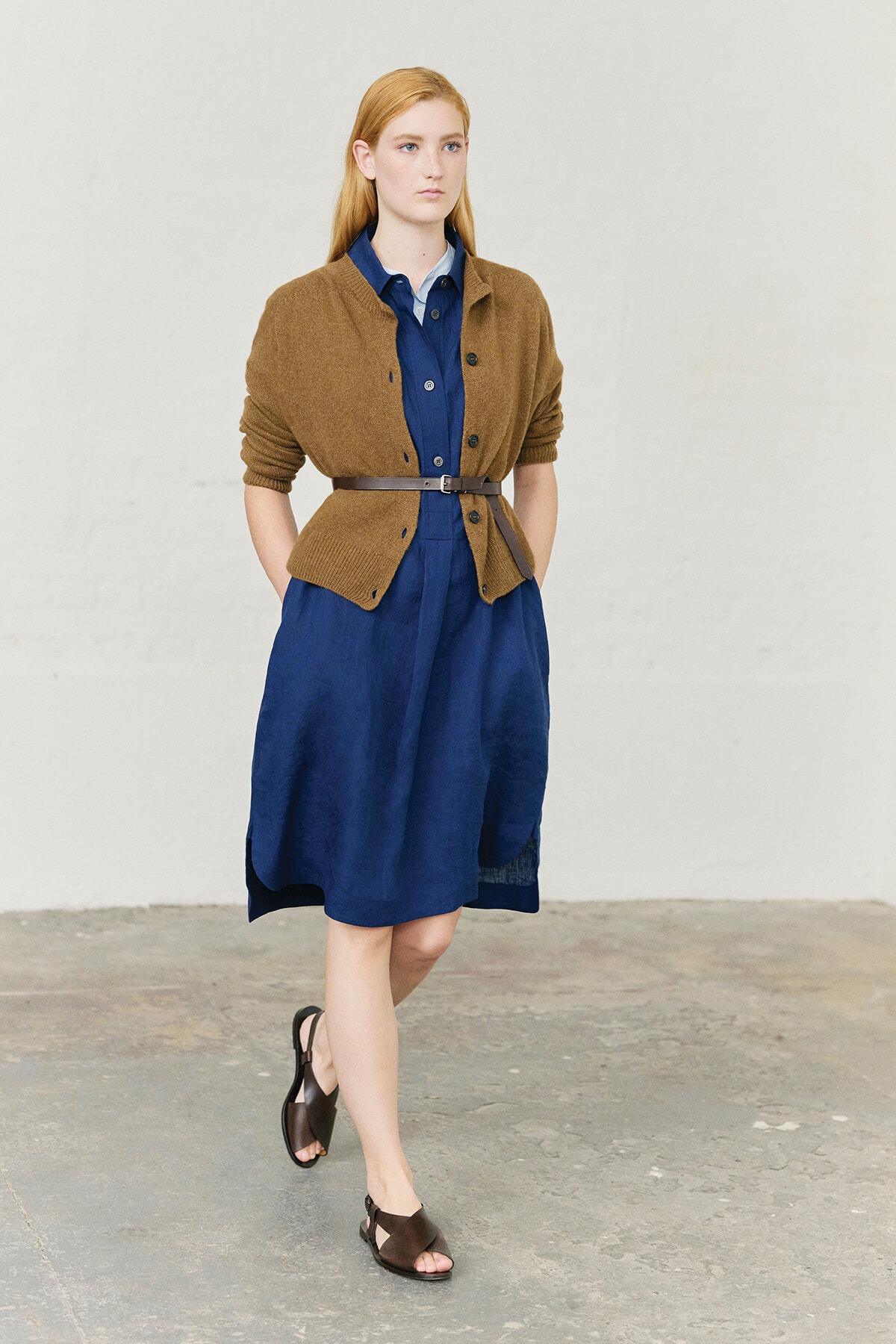Woman in a navy blue dress with a brown cardigan belted at the waist, walking indoors.