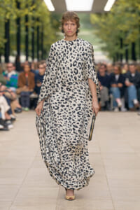 models walks a monochrome leopard-print flowing gown down a runway in an outdoor fashion show.