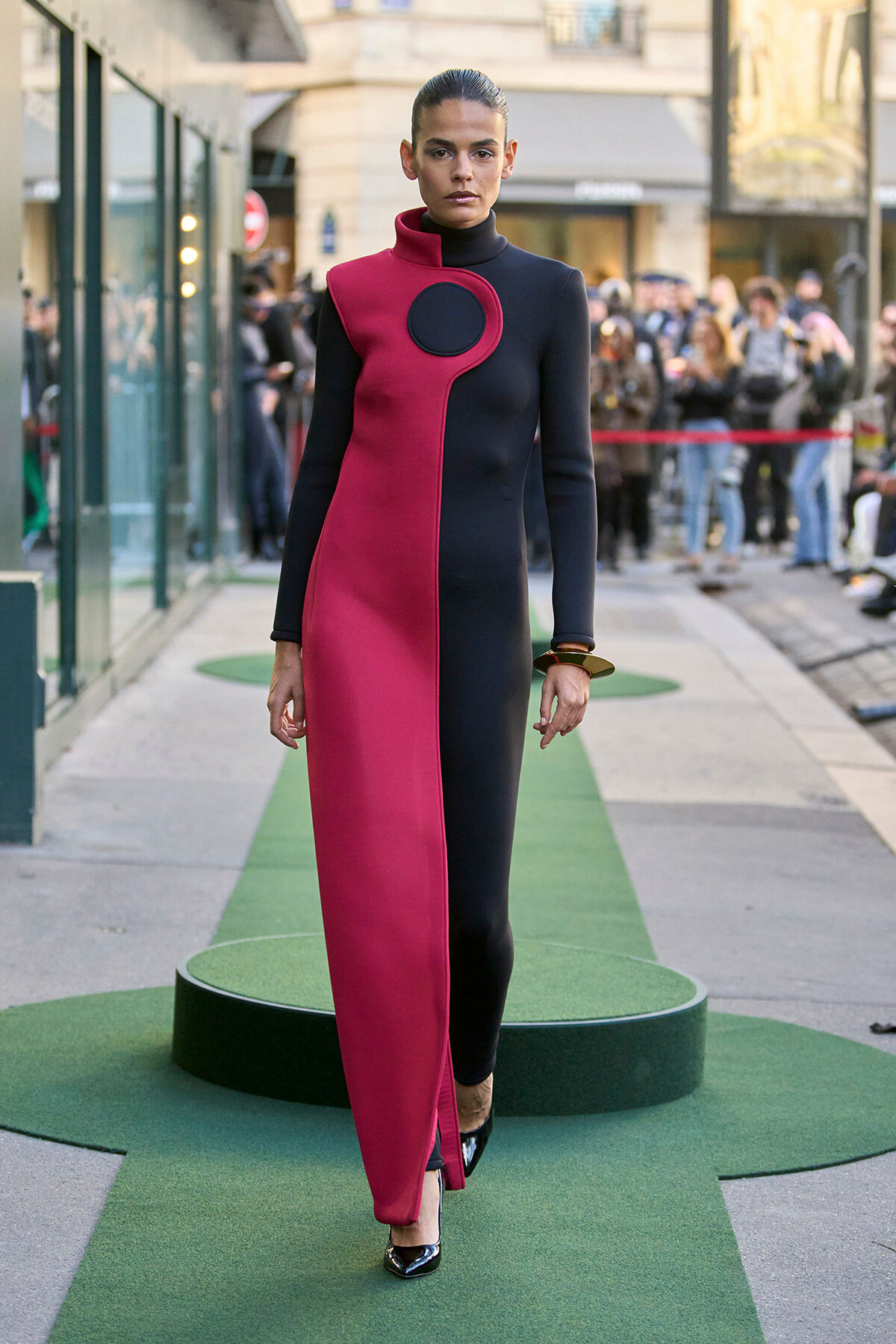 Model walking a city runway in a two-tone black and magenta color-block gown with a circular black accent at the collar area.