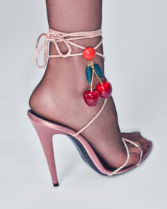 Pink stiletto heel with wrap-around ankle straps and cherry charm on sheer hosiery.