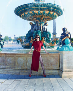 Woman in a red dress posing at a large ornate fountain with water spraying around her.