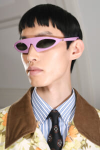 Person wearing pink futuristic sunglasses with a black bowl cut and floral jacket.