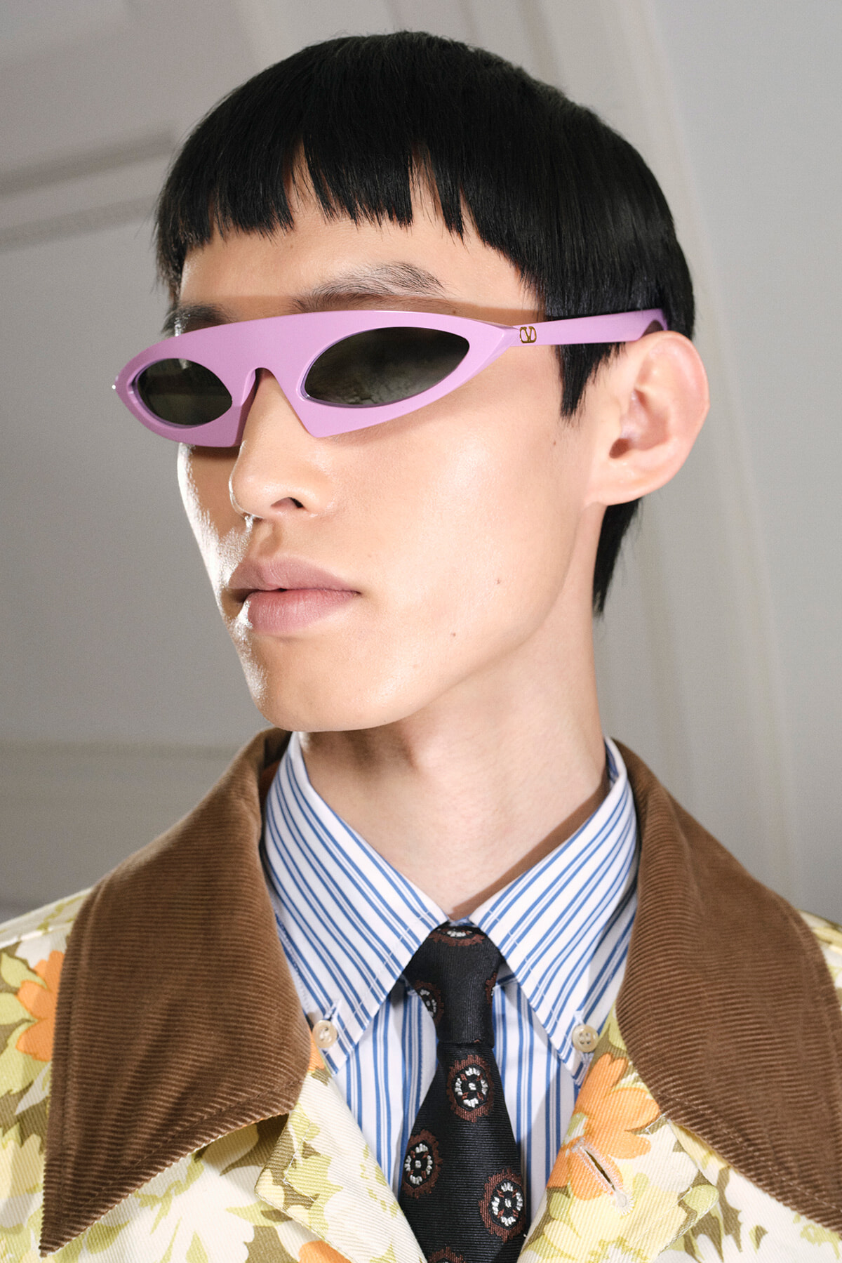 Person wearing pink futuristic sunglasses with a black bowl cut and floral jacket.