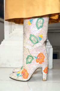 Knee-high boot covered in pale pink sequins with bright orange and turquoise floral embroidery on a white floor.