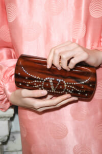 Brown glossy clutch decorated with rhinestones in a crown design, held by a person in a pink patterned dress.