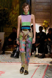 Model walking a runway in a color-block sleeveless top and multicolored abstract-print pants, carrying a black handbag.