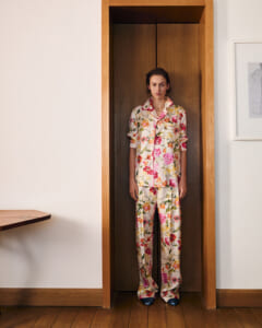 Person standing in a tall wooden doorway wearing a cream floral pajama set with pink and yellow flowers, hands at sides.