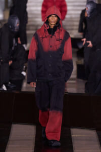 Model wearing a red-to-black gradient hooded jacket with matching cargo pants on a fashion runway., Female model in a color-block red and black parka with oversized pockets walking the catwalk., Runway look featuring a red-to-black gradient hooded jacket and loose cargo pants., Fashion show model in an urban-inspired red-dipped parka and black pants, walking the runway., Gradient red and black outerwear with hood, paired with wide cargo trousers, on a fashion show.