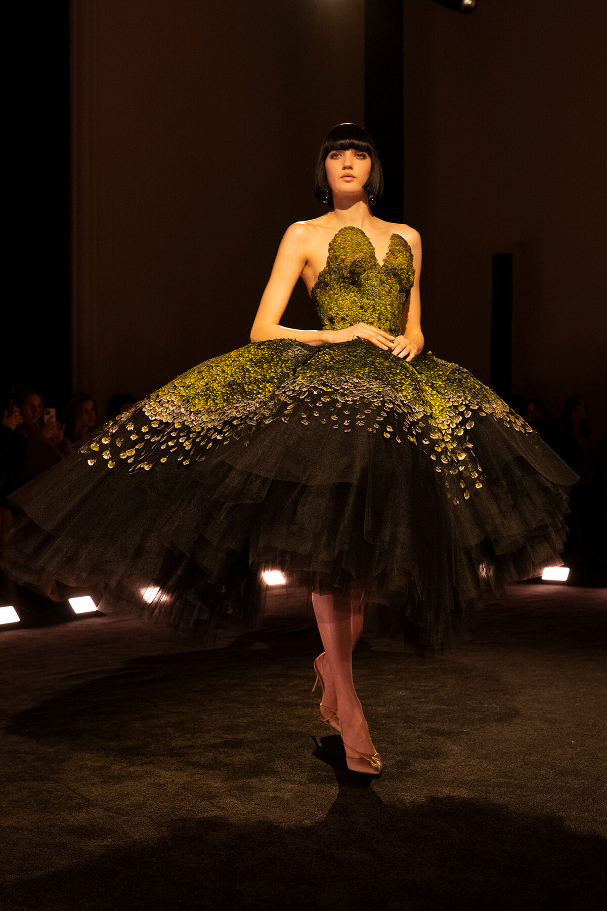 Model walks the runway in a dramatic emerald-green gown with a mossy-scale bodice and a voluminous black tulle skirt.