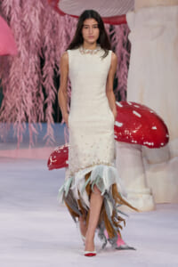 Model walks the runway in a sleeveless cream textured dress with a feathered, multicolored fringe hem.