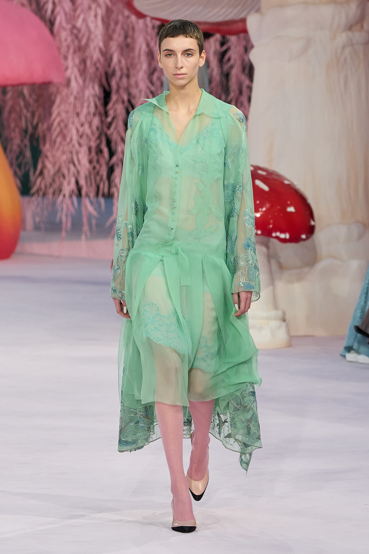 Model walking a runway in a sheer mint-green blouse and matching layered skirt with delicate embroidery.