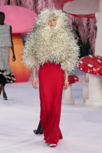 Model walks the runway in a voluminous cream spiky wraps over red wide-leg pants, creating a bold fashion statement.