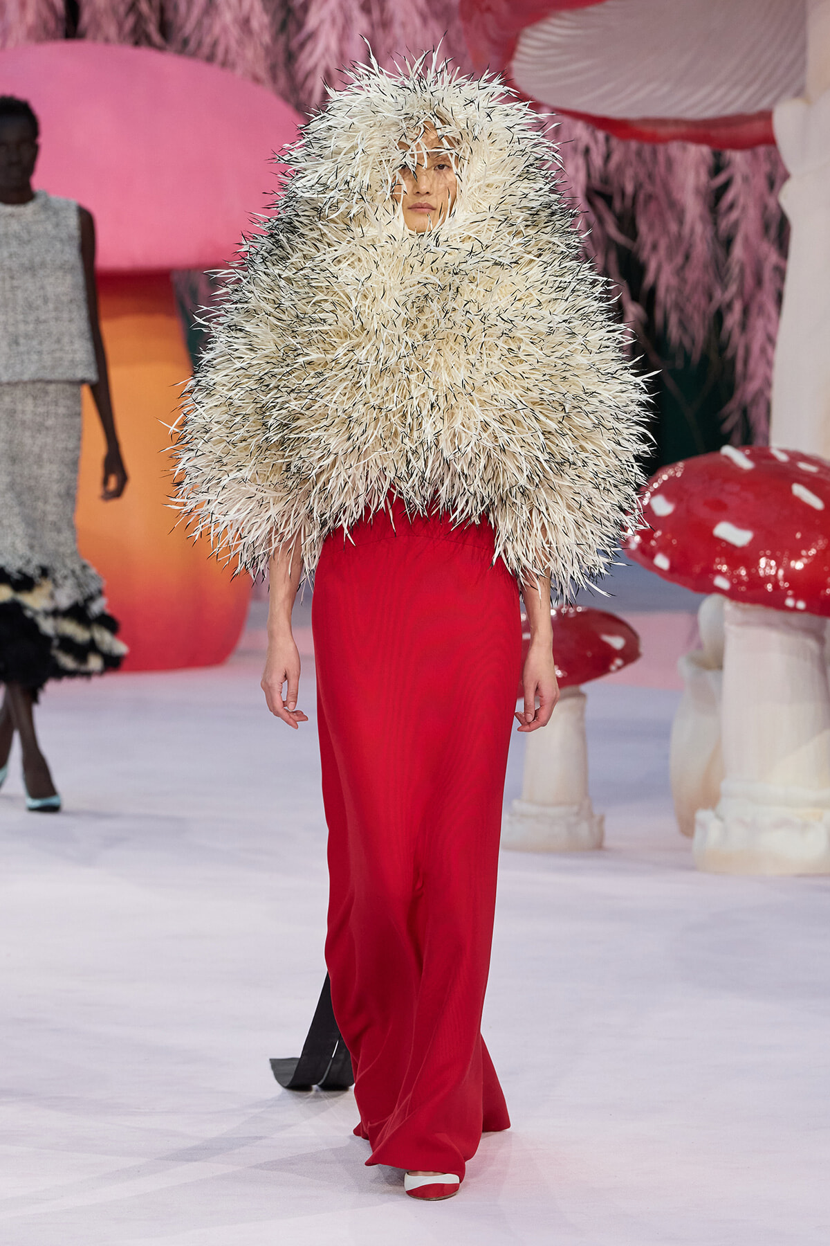 Model walks the runway in a voluminous cream spiky wraps over red wide-leg pants, creating a bold fashion statement.