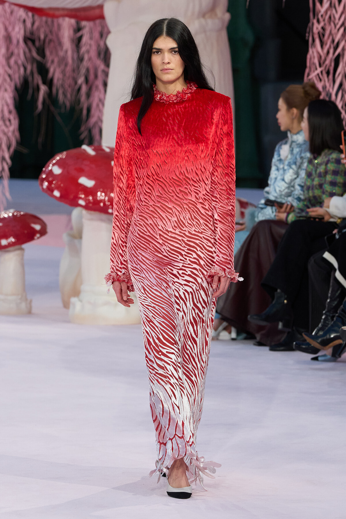 Model walks runway in a long red-to-white zebra-printed dress with ruffled high neck and cuffs. Or concise: Model on runway wearing a gradient red-to-white zebra print gown with ruffle details.