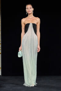 Model on a runway wearing a strapless black gown with a sparkling mint-beaded overlay and a mint clutch.