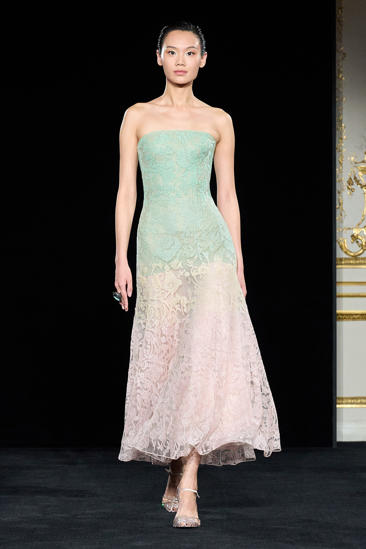 Strapless pastel lace gown on a model, gradient from mint green to pale pink, mid-runway pose.