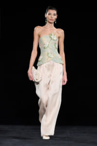Model walking runway in strapless, mint-green embellished top and wide ivory trousers, carrying a cream clutch.
