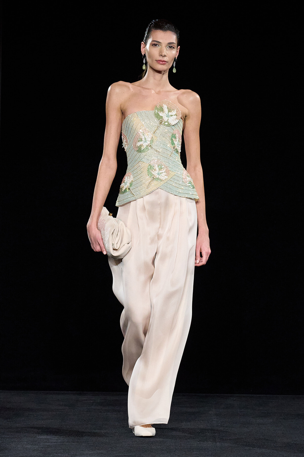 Model walking runway in strapless, mint-green embellished top and wide ivory trousers, carrying a cream clutch.