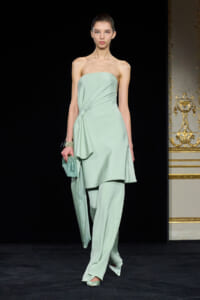 Model on a runway wearing a strapless mint-green draped ensemble with a side gathered detail and matching pants, holding a mint clutch.