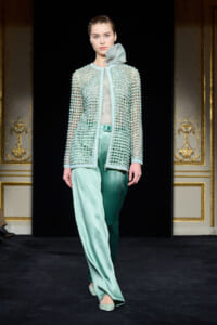 Model walking a runway in a mint-green beaded cardigan over a sheer top with satin wide-leg pants.