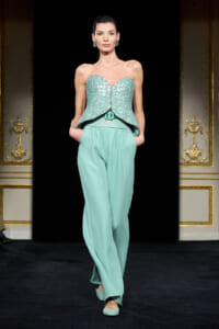 Model on a runway wearing a turquoise strapless beaded peplum top and wide-leg pants with matching flats.
