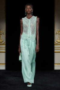 Model on a runway wearing a mint-green beaded sleeveless top with cascading beadwork and matching wide-leg satin pants, carrying a mint clutch.