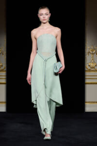 Model on runway wearing a mint strapless beaded bodice top with a matching high-low skirt, holding a small mint clutch.