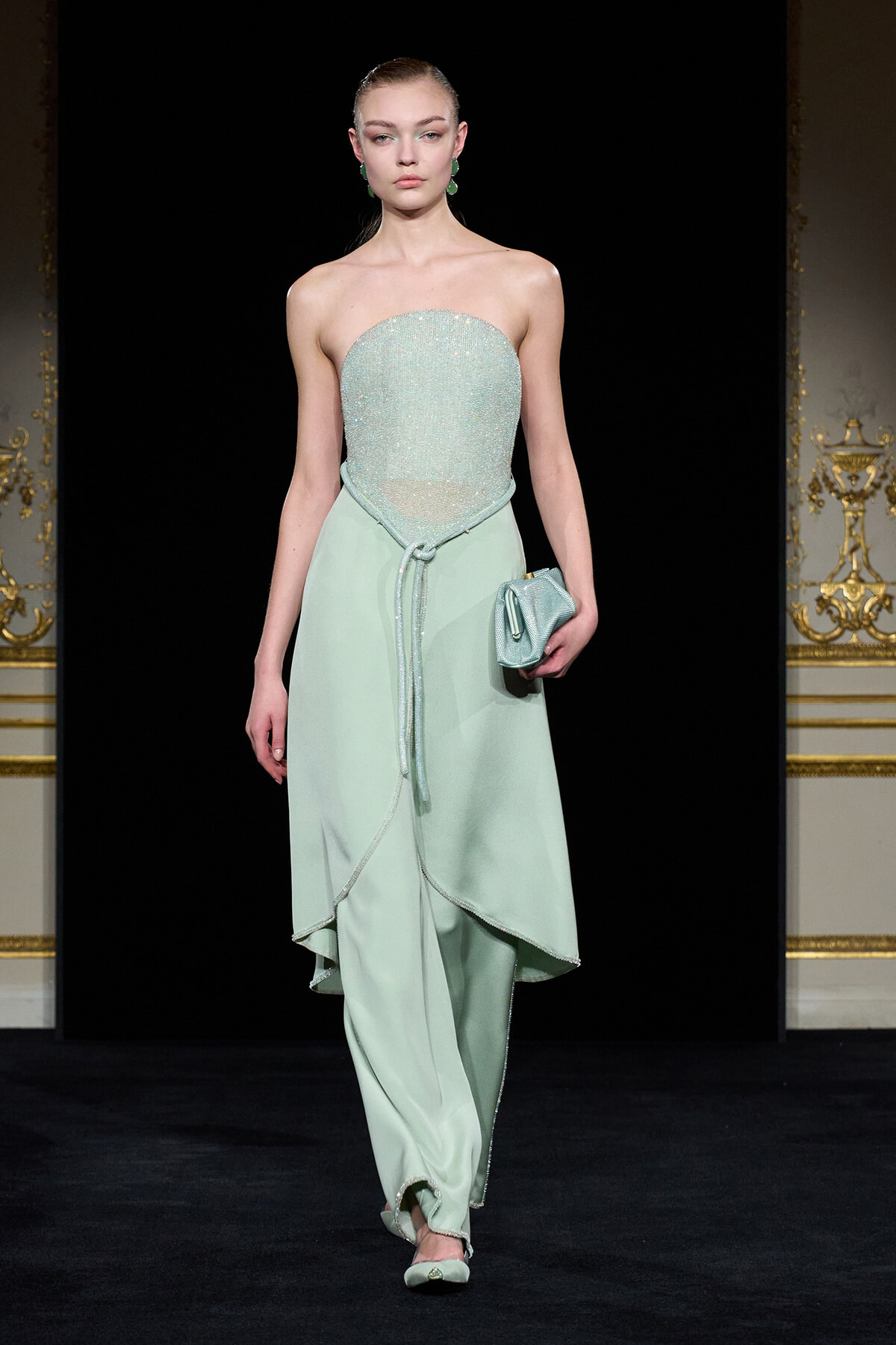 Model on runway wearing a mint strapless beaded bodice top with a matching high-low skirt, holding a small mint clutch.