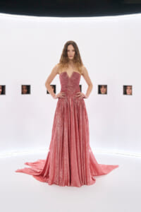Model wearing a sparkling pink strapless gown with a long train, standing against a white studio backdrop.