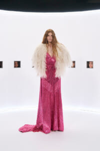 Model wearing a pink sequin gown with a fluffy white fur cape in a stark white studio backdrop.