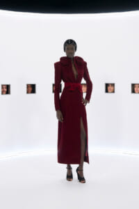 Model in burgundy velvet gown with oversized rose-shoulder details, bow belt, and high slit, posing in a white studio with square window frames showing faces