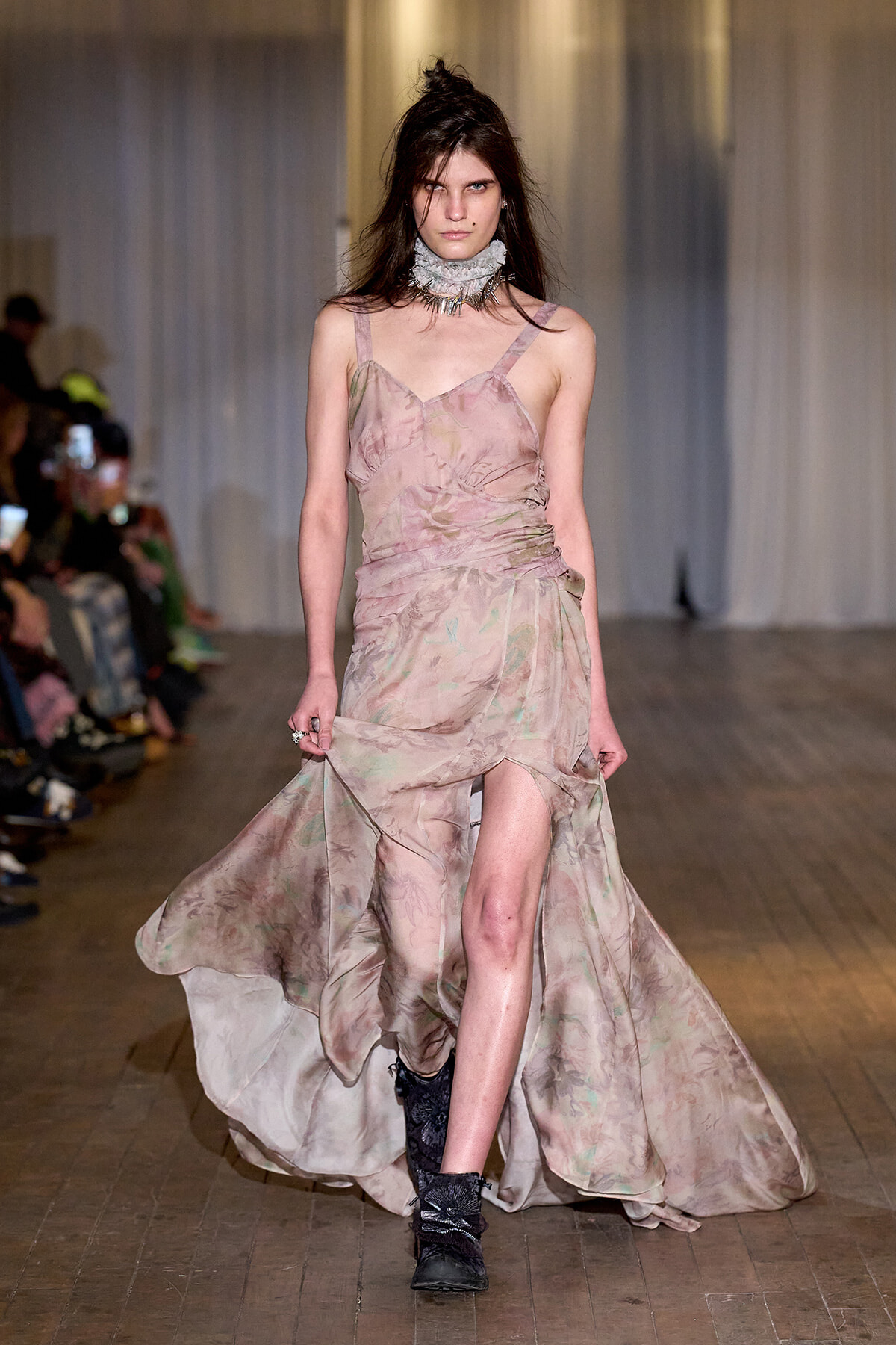 Model walking a runway in a flowing pink floral gown with a high slit, paired with black ankle boots and a layered choker.