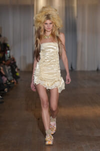 Runway model wearing ivory satin strapless mini dress with ruched sides and a layered ruffle hem, on a fashion catwalk.