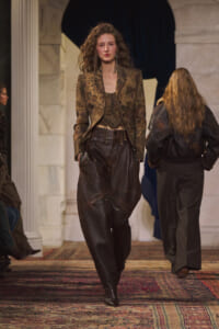 Model on a runway wearing a brown floral-patterned blazer with a matching corset and baggy dark leather pants