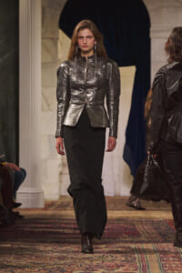 Model walks the runway in a metallic silver tailored jacket with a peplum over black wide-leg pants and ankle boots.