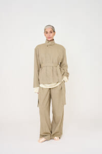 Model wearing a beige belted knit jacket and matching wide-leg pants in a neutral studio setting, tan-toned layered look.