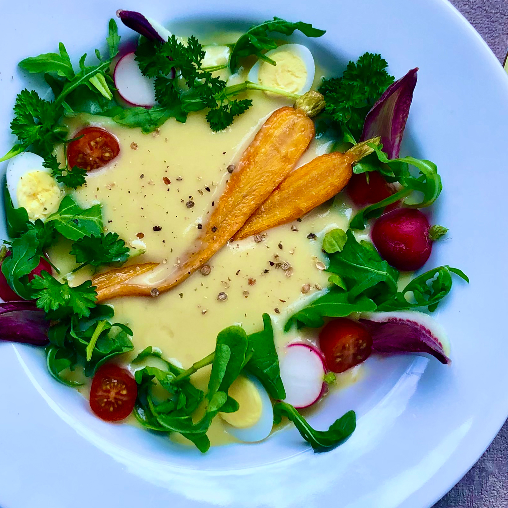 Green salad with mixed leaves, radishes, cherry tomatoes, sliced hard-boiled eggs, carrot chips, and fresh herbs with a creamy yellow dressing.