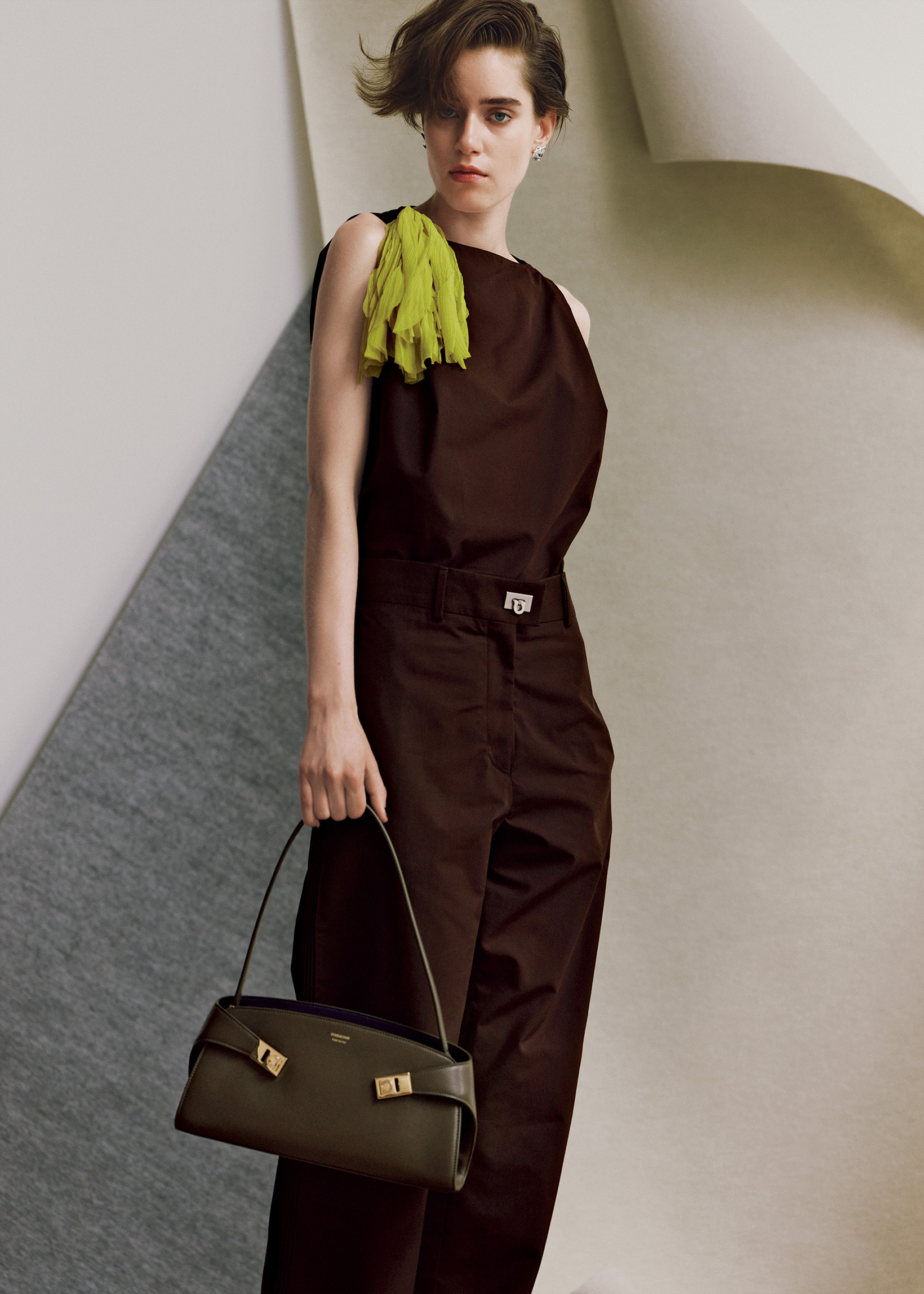 ferragamo-04-260717 | madameFIGARO.jp(フィガロジャポン) シックなコーヒーブラウンのワントーンに、肩に飾ったサルファーイエローのコサージュが鮮やかに映える。パンツのウエストにはアイコンのガンチーニをさりげなく光らせて、横長フォルムがグラフィカルな新作バッグ「ハグ イーストウエスト」をフレッシュにスタイリングする。コサージュ付きトップ¥170,500、パンツ¥176,000、ピアス¥59,400、バッグ「ハグ イーストウエスト」¥341,000/以上フェラガモ(フェラガモ・ジャパン)