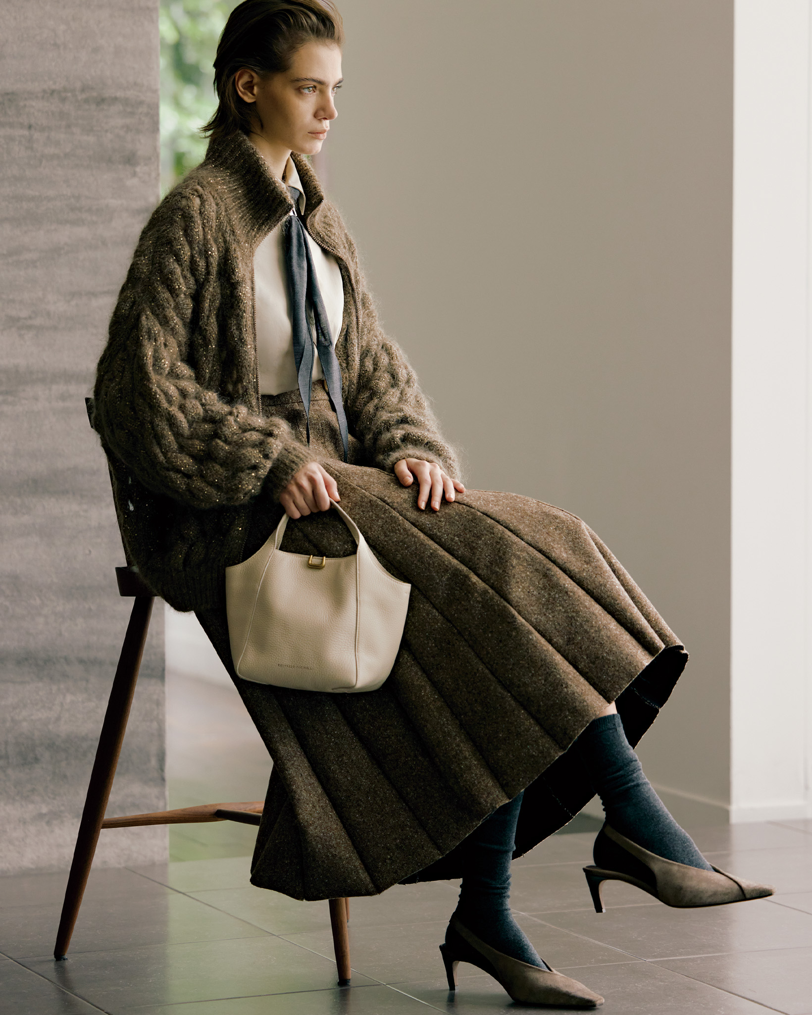 02-brunellocucinelli-260820 | madameFIGARO.jp(フィガロジャポン) ブルネロ クチネリの2026年秋冬コーディネート2枚目。バッグ「サルトリアル バケットバッグ」(ストラップ付き)¥533,500、ニットカーディガン¥594,000、シャツ¥388,300、スカート¥570,900、スカーフ¥57,200、シューズ¥273,900/以上ブルネロ クチネリ(ブルネロ クチネリ ジャパン) ソックス/スタイリスト私物