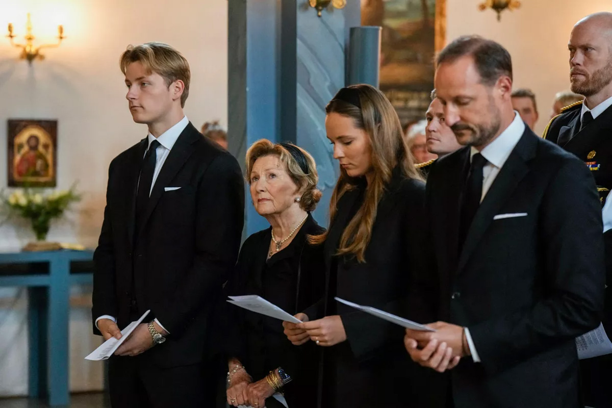 Group of formally dressed people standing in a church, holding programs during a ceremony.