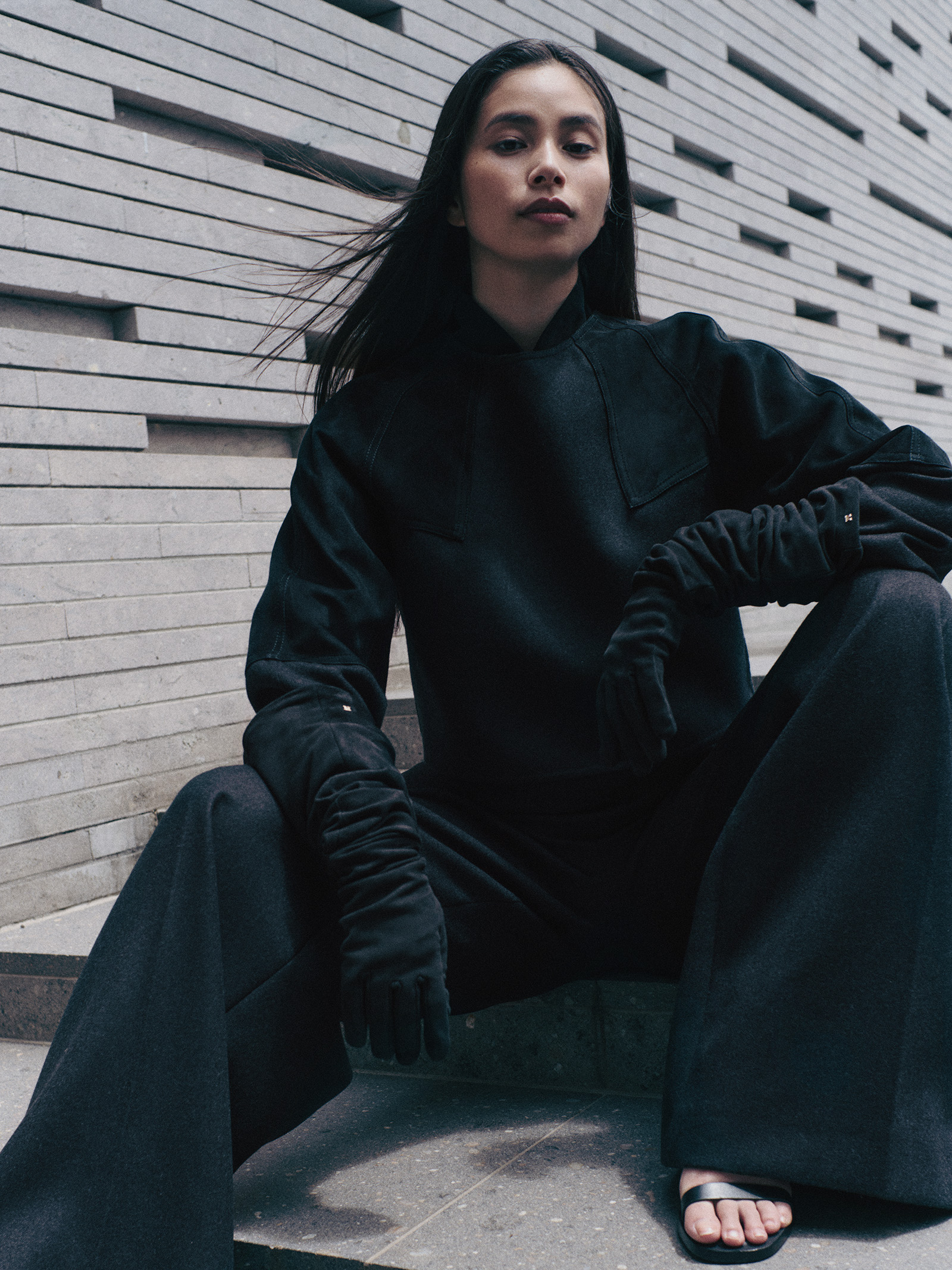 260831-yuiko-kawauchi-maxmara-06 | madameFIGARO.jp(フィガロジャポン) Portrait of a young woman in a black outfit sitting on concrete steps, looking at the camera.
