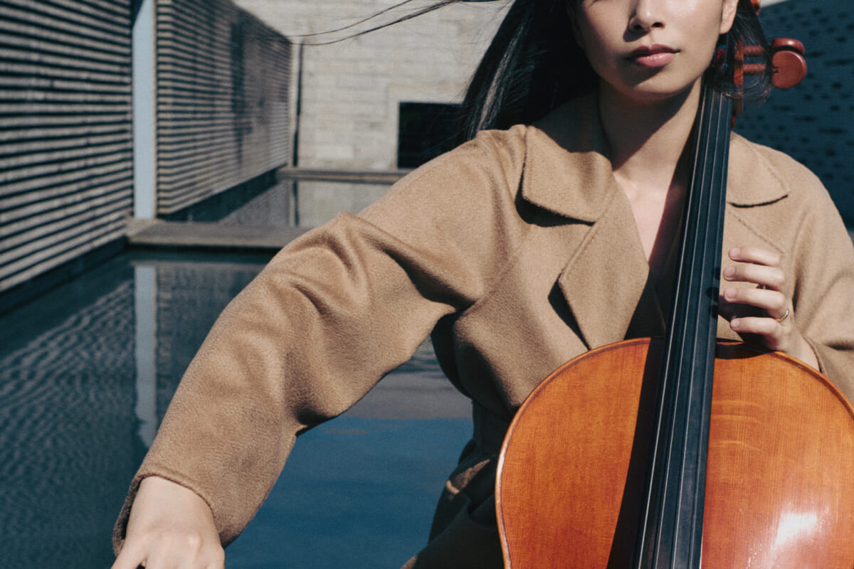 Woman playing a cello outdoors, bow drawn across strings with focus on her hands and instrument's wood finish.