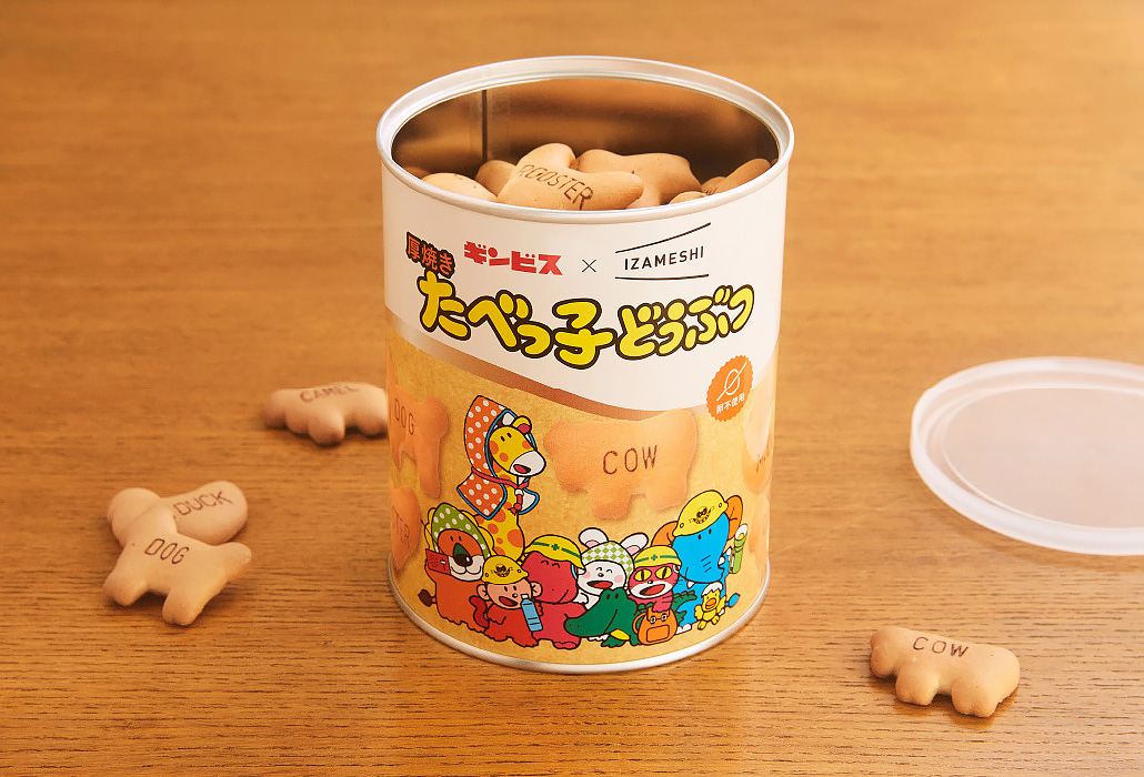 Open tin of bone-shaped dog biscuits on a wooden table; biscuits stamped with 'DOG' and 'COW' beside the can; colorful cartoon label.