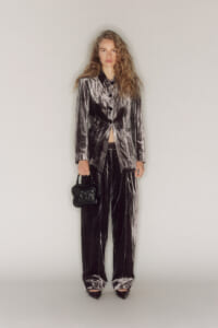 Model in a metallic velvet suit: cropped blazer with matching wide-leg pants, holding a small black handbag against a neutral studio backdrop