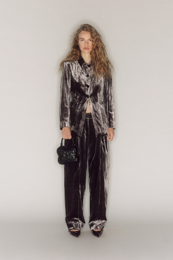 Model in a metallic velvet suit: cropped blazer with matching wide-leg pants, holding a small black handbag against a neutral studio backdrop