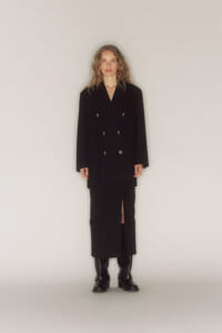 Full-length view of a person in a black double-breasted blazer and midi skirt with a front slit, wearing black ankle boots.