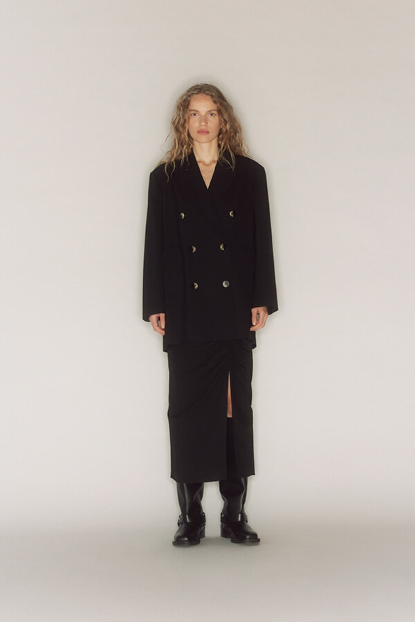 Full-length view of a person in a black double-breasted blazer and midi skirt with a front slit, wearing black ankle boots.