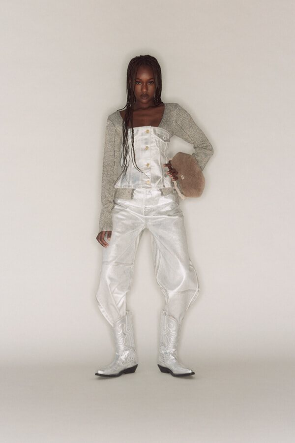 Model wearing a metallic white co-ord: cropped corset top with long-sleeve cardigan, high-waisted pants, white boots, and a beige fuzzy hat.