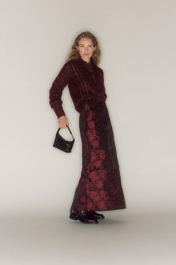 Model wearing a burgundy lace sweater and matching floral lace maxi skirt, holding a small black handbag.